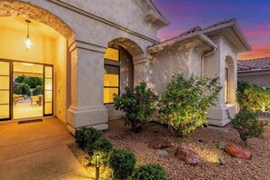 A building with a stone facade, arched doorways, and a landscaped garden with rocks and shrubs.