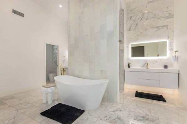 A modern bathroom with a freestanding bathtub, a vanity with a mirror, and a marble floor.