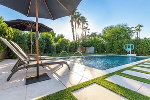 A pool area with a lounge chair, umbrella, and a basketball hoop.
