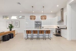 A modern kitchen with white cabinets, a central island with bar stools, pendant lighting, and a stainless steel refrigerator. - Anderson LUX Estate/Private Bar&Pool/Sleeps 12 (Scottsdale)