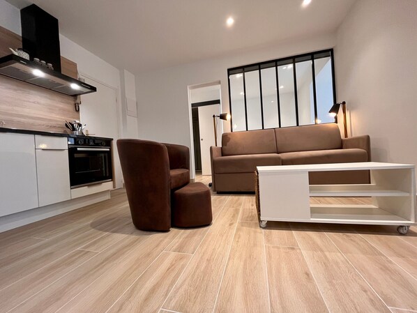 A modern living room with a sofa, a coffee table, and a kitchen area with a stove and cabinets.