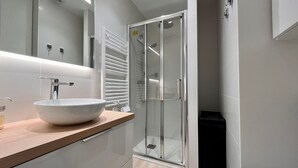Un baño moderno con un lavamanos grande de color blanco, una mampara de ducha de vidrio y un mueble de tocador de madera.