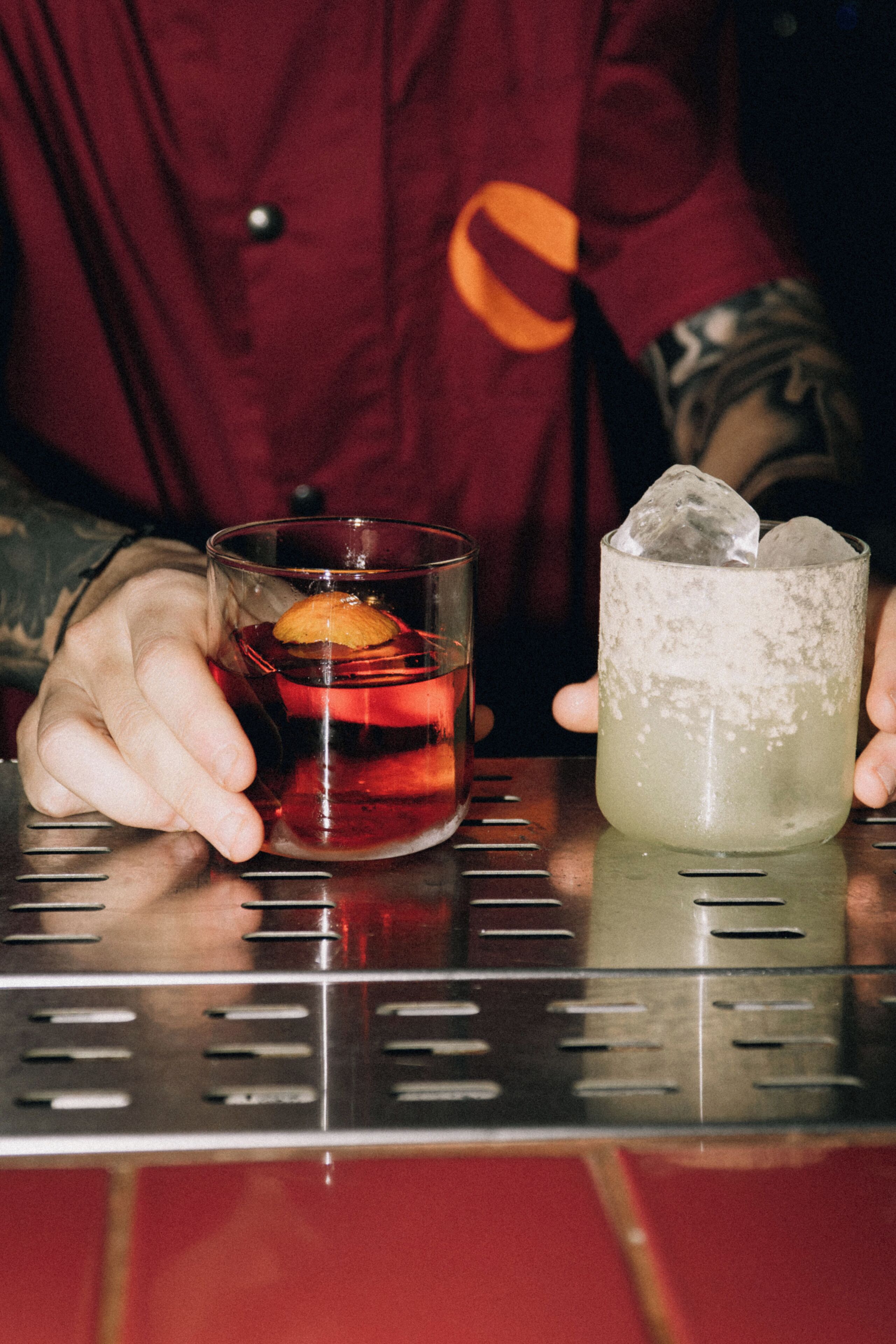 Une personne tenant deux verres de boissons sur le comptoir d’un bar.