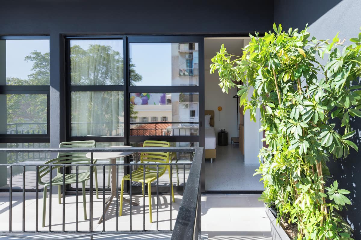 A modern outdoor seating area with a table and chairs, a potted plant, and a view of the building's interior through large windows.