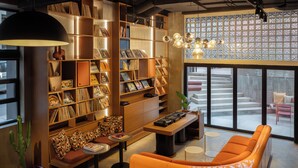 A modern interior with a wooden bookshelf, orange sofa, and a dining area. - Okupa (Athens)