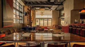 A spacious indoor area with a long table, multiple chairs, a sofa, and a bar area. - Okupa (Athens)