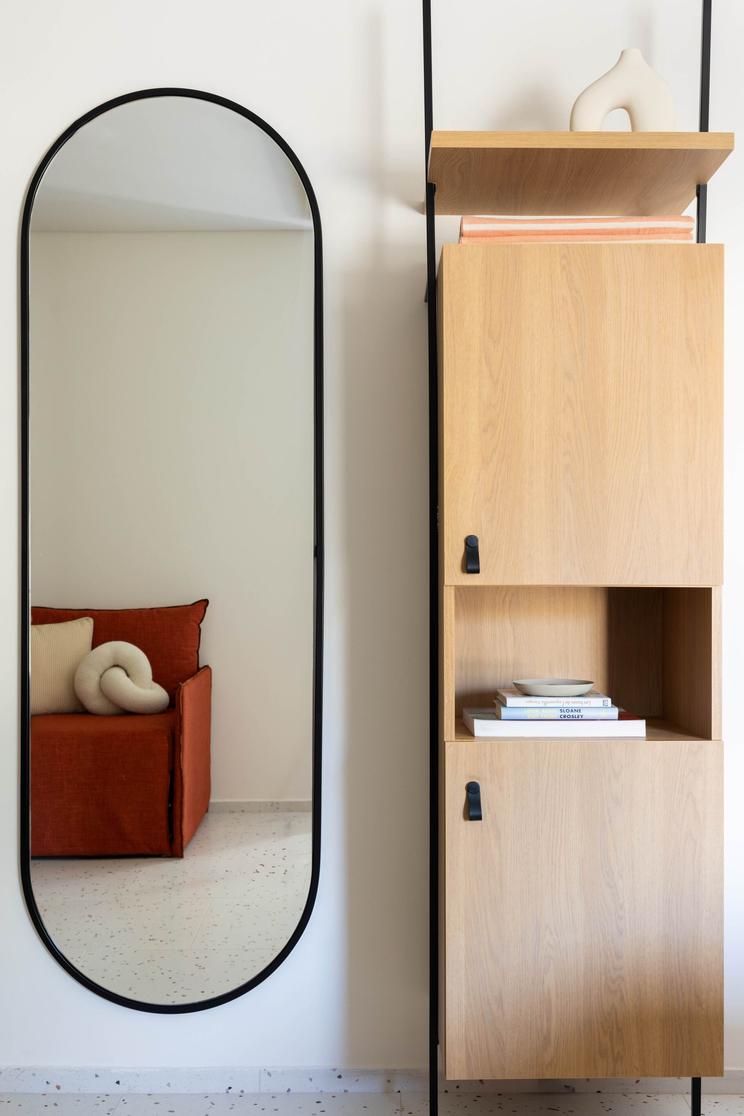 Una habitación con un espejo grande, un mueble de madera con estantes y un sofá rojo con un cojín blanco.