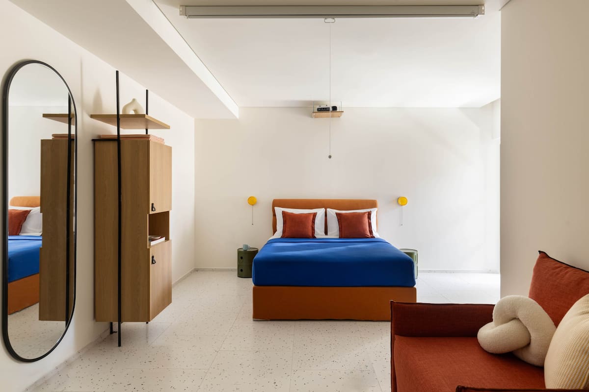 A modern bedroom with a bed, a wardrobe, a mirror, and a hanging light fixture.