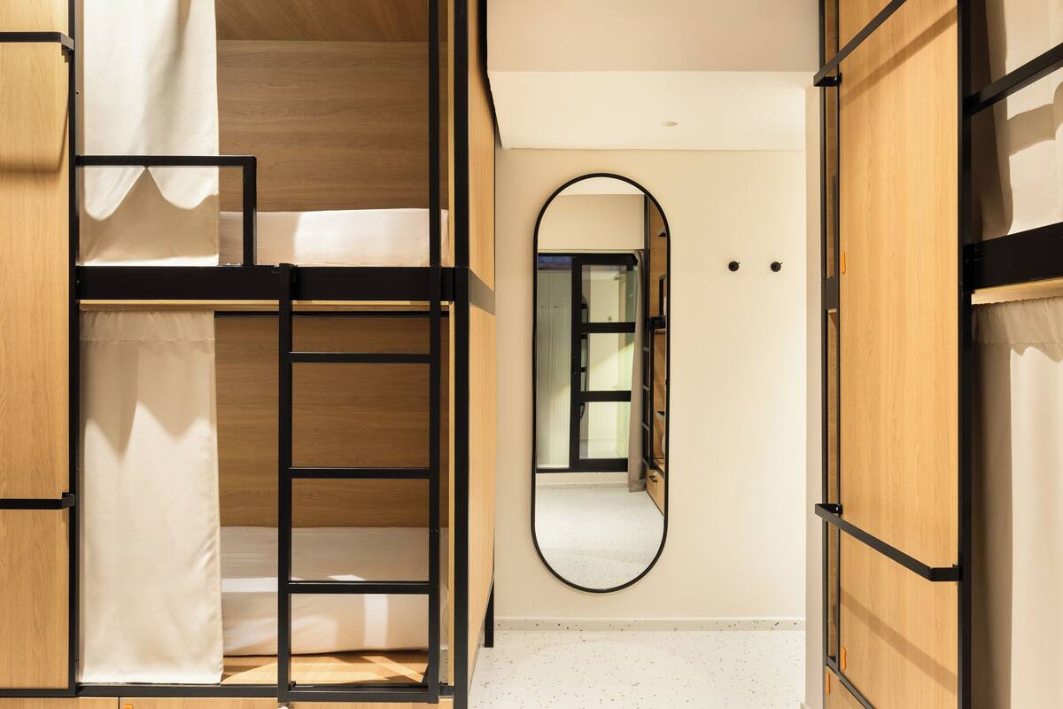 A bedroom with a bunk bed, a wooden wardrobe, a mirror, and a door leading to another room.