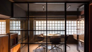 A modern meeting room with a glass partition, wooden bookshelves, and a round table with chairs. - Okupa (Athens)