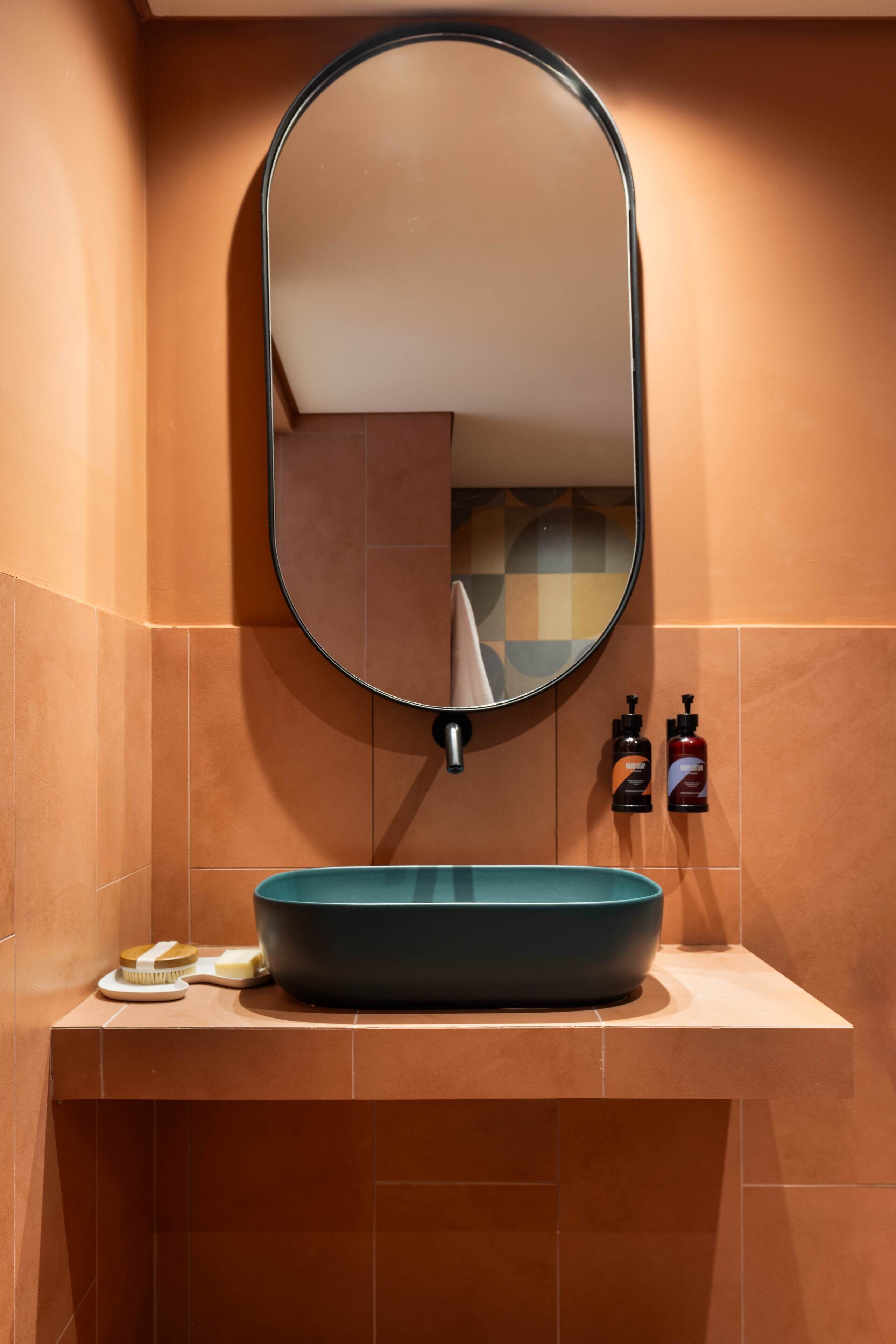 A bathroom with a round mirror, a blue sink, and two bottles of soap on the wall.