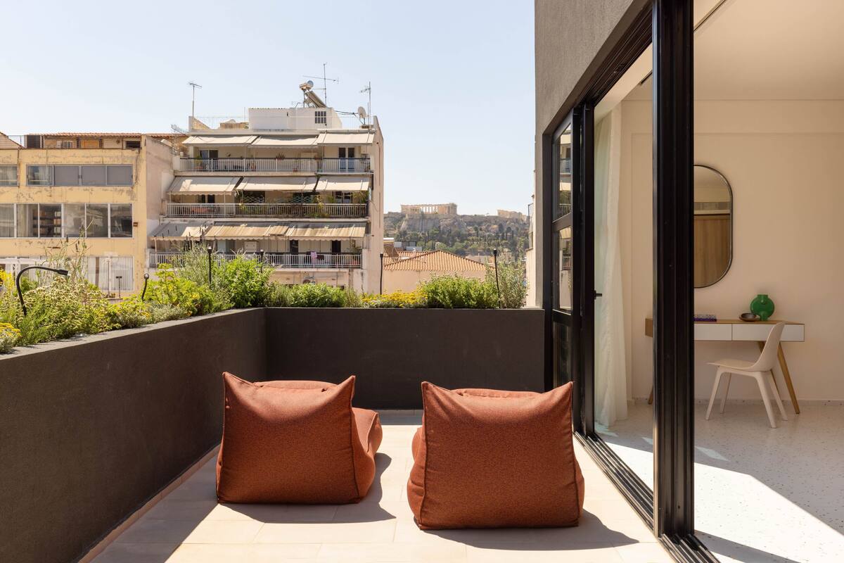 A balcony with two brown cushions, a white chair, and a desk with a mirror and a green vase.