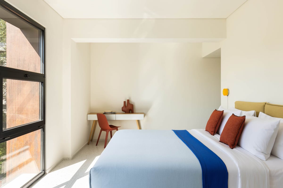 A modern hotel room with a large bed, a desk, and a chair.