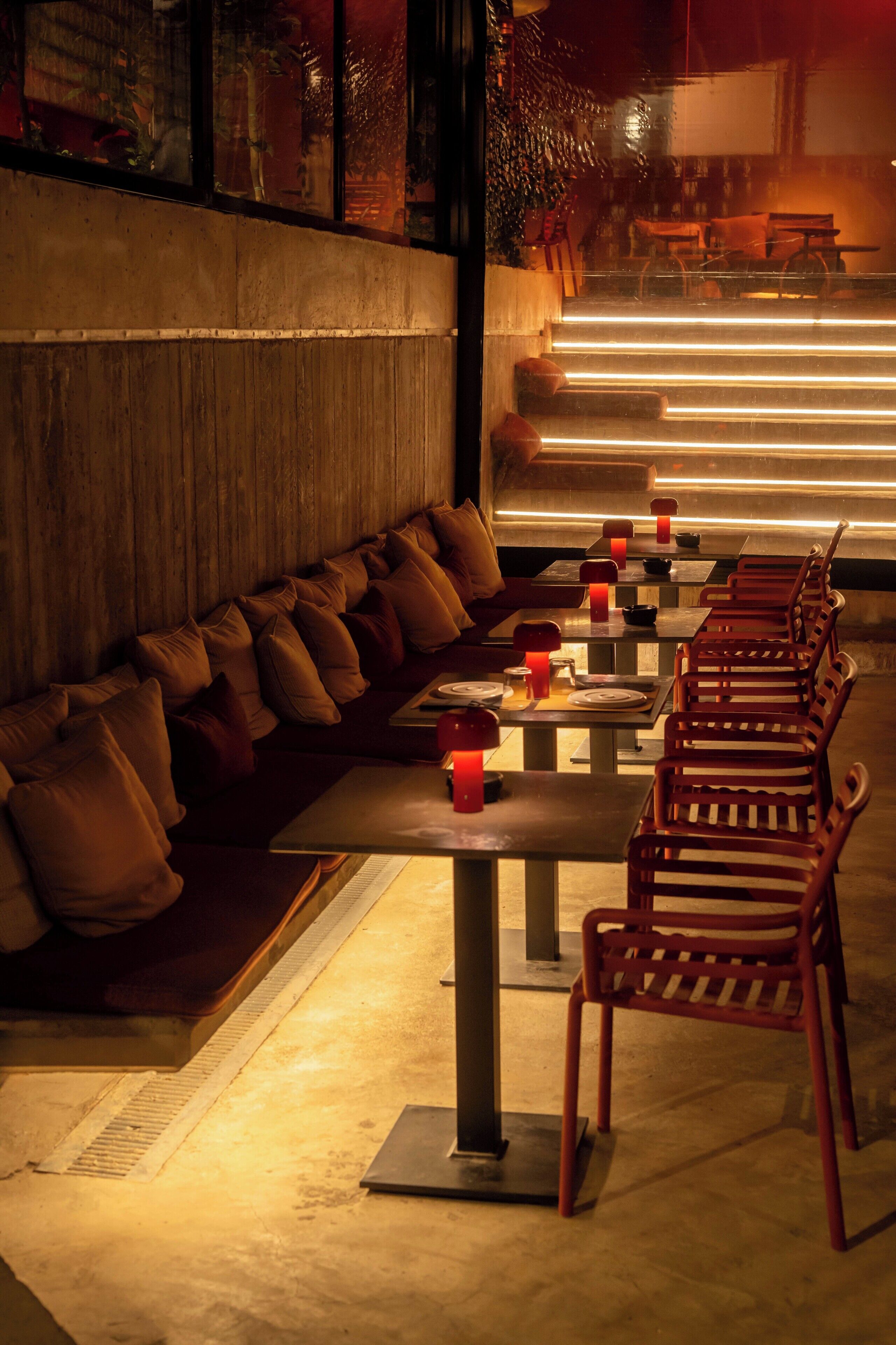 A restaurant with a long counter, cushioned seating, and tables with red candle-like lights.