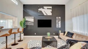 Una sala moderna con un televisor negro grande, un sofá, una mesa de centro y una alfombra estampada.