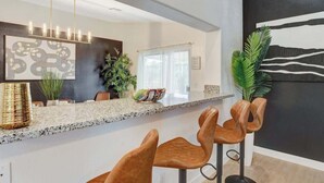 Una cocina moderna con encimera de granito, taburetes de bar y una lámpara colgante.