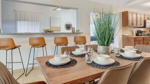 Un comedor con una mesa de madera dispuesta para cuatro personas, rodeada de sillas marrones. Un gran macetero se encuentra en el centro.