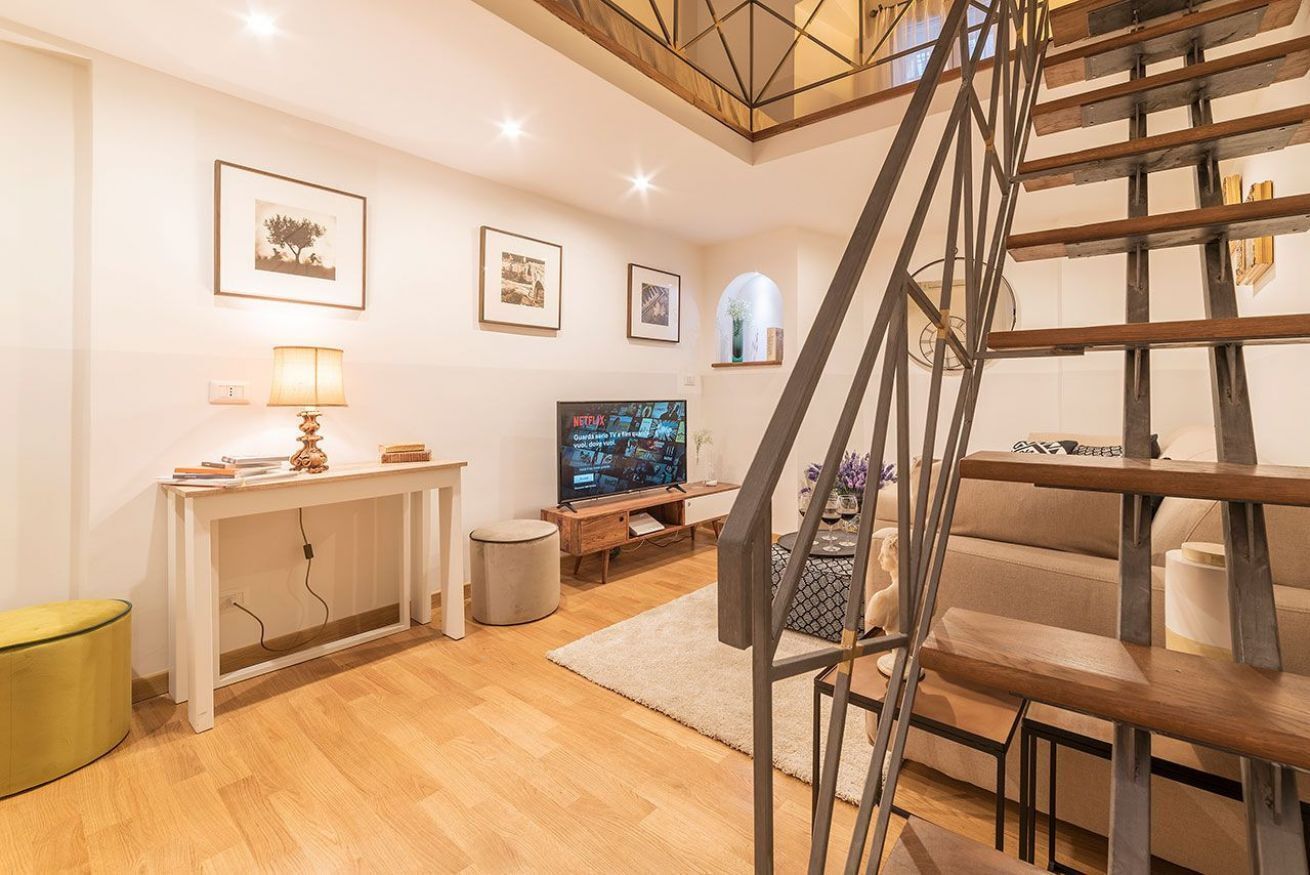 Un salon moderne avec un escalier en bois, un téléviseur, une console et des tableaux encadrés accrochés au mur.