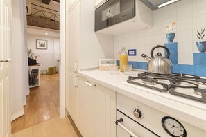 A kitchen with white cabinets, a gas stove, a kettle, and a microwave. - Campo de’ Fiori 35 - modern and quiet, in the center of Rome (Roma)
