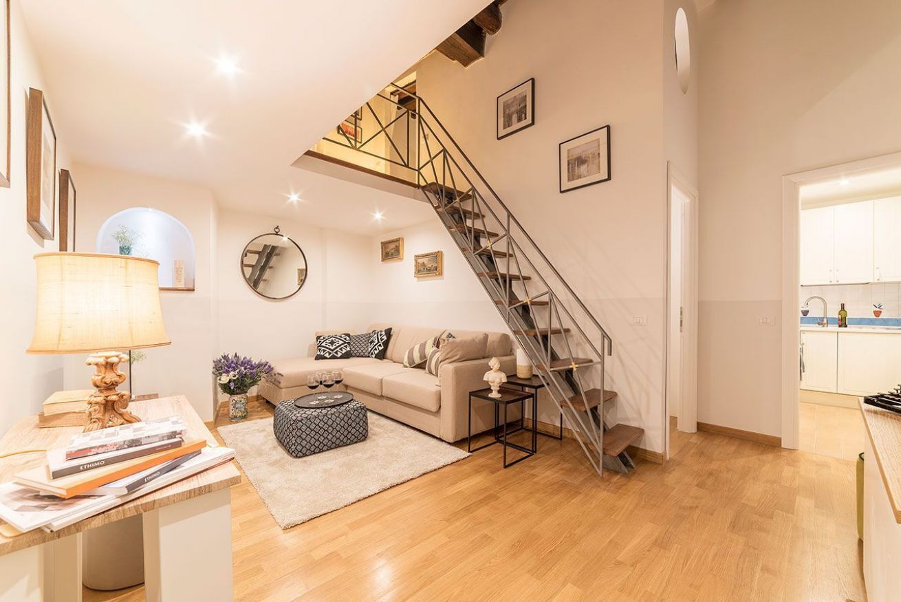 A modern living room with a staircase leading to an upper floor, a sofa, a coffee table, and a lamp.