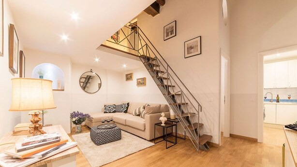 A modern living room with a staircase leading to an upper floor, a sofa, a coffee table, and a lamp.