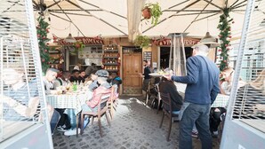 An outdoor café with tables and chairs, a man serving food, and a sign for 'Cucina Romana'.