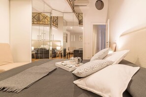 A modern bedroom with a large bed, a bedside table with a tray of breakfast items, and a view into the living area through a glass partition. - Campo de’ Fiori 35 - modern and quiet, in the center of Rome (Roma)