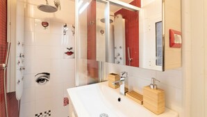 A modern bathroom with a glass shower enclosure, a white sink with a wooden soap holder, and a mirror above the sink.