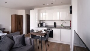 A modern kitchen with white cabinets, a microwave, and a sink. There is a dining area with a table and chairs. - Stay Zeni, Alexandra Rise Manchester Chic Studio (Manchester)