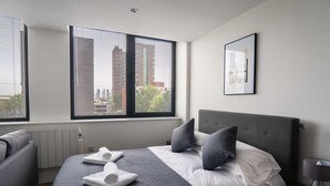 A modern hotel room with a large bed, grey bedding, and a view of the city through floor-to-ceiling windows. - Stay Zeni, Alexandra Rise Manchester Chic Studio (Manchester)