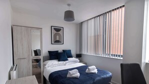 Une chambre d’hôtel moderne équipée d’un grand lit, d’un bureau, d’une chaise, d’une armoire et d’une fenêtre avec des stores.