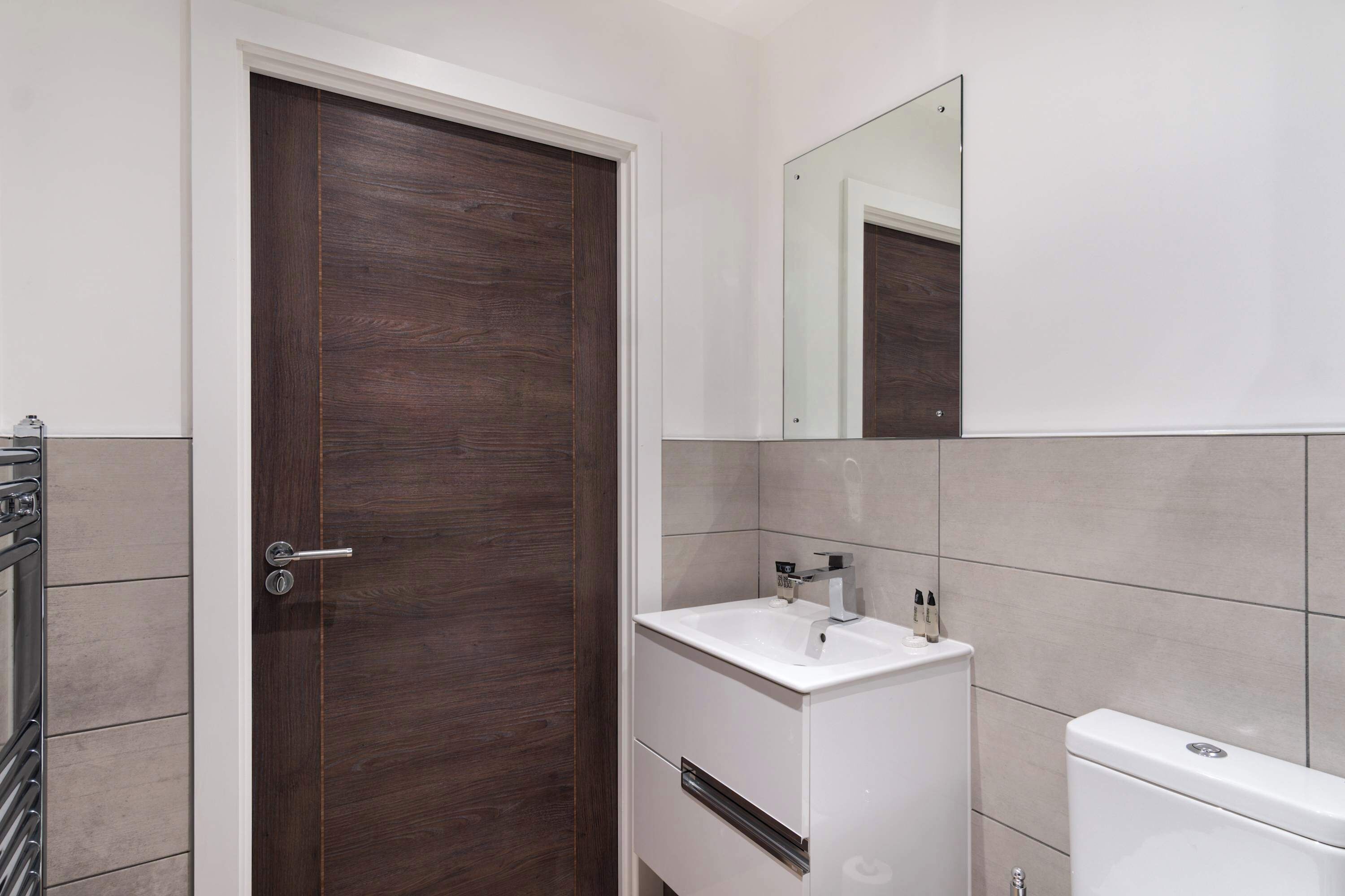 Une salle de bain avec une porte en bois foncé, un lavabo blanc et un miroir au-dessus.
