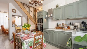 Een keuken met een eetgedeelte, met een trap, houten stoelen, een tafel met geruit tafelkleed en een kroonluchter.