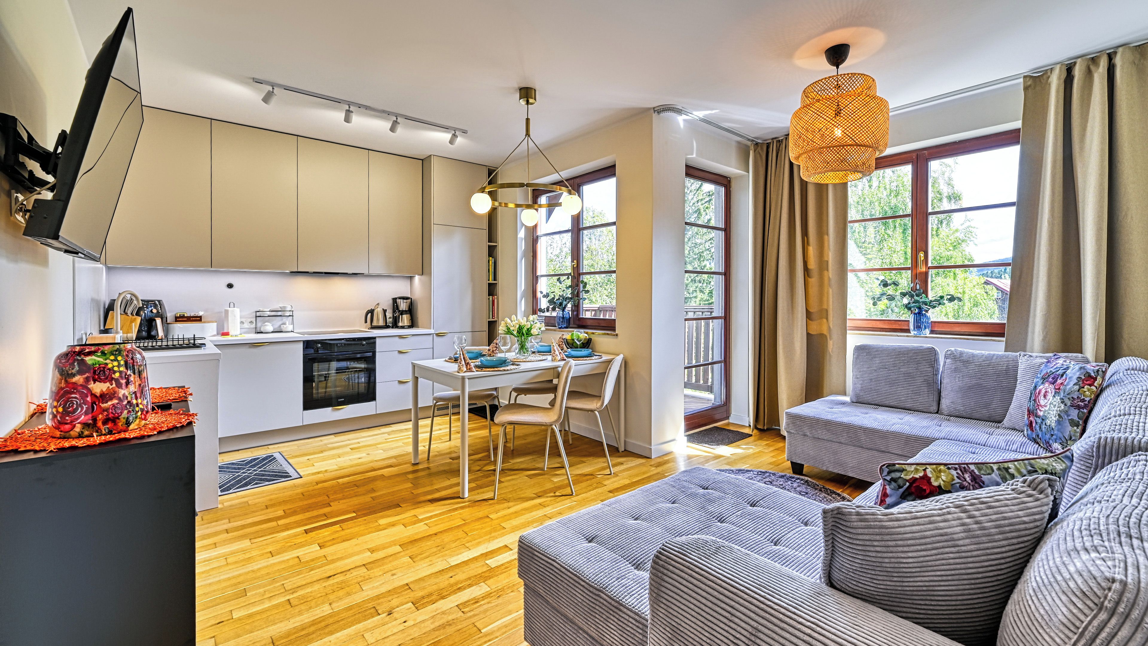 A modern kitchen with a dining area, a sofa, and a large window with curtains.