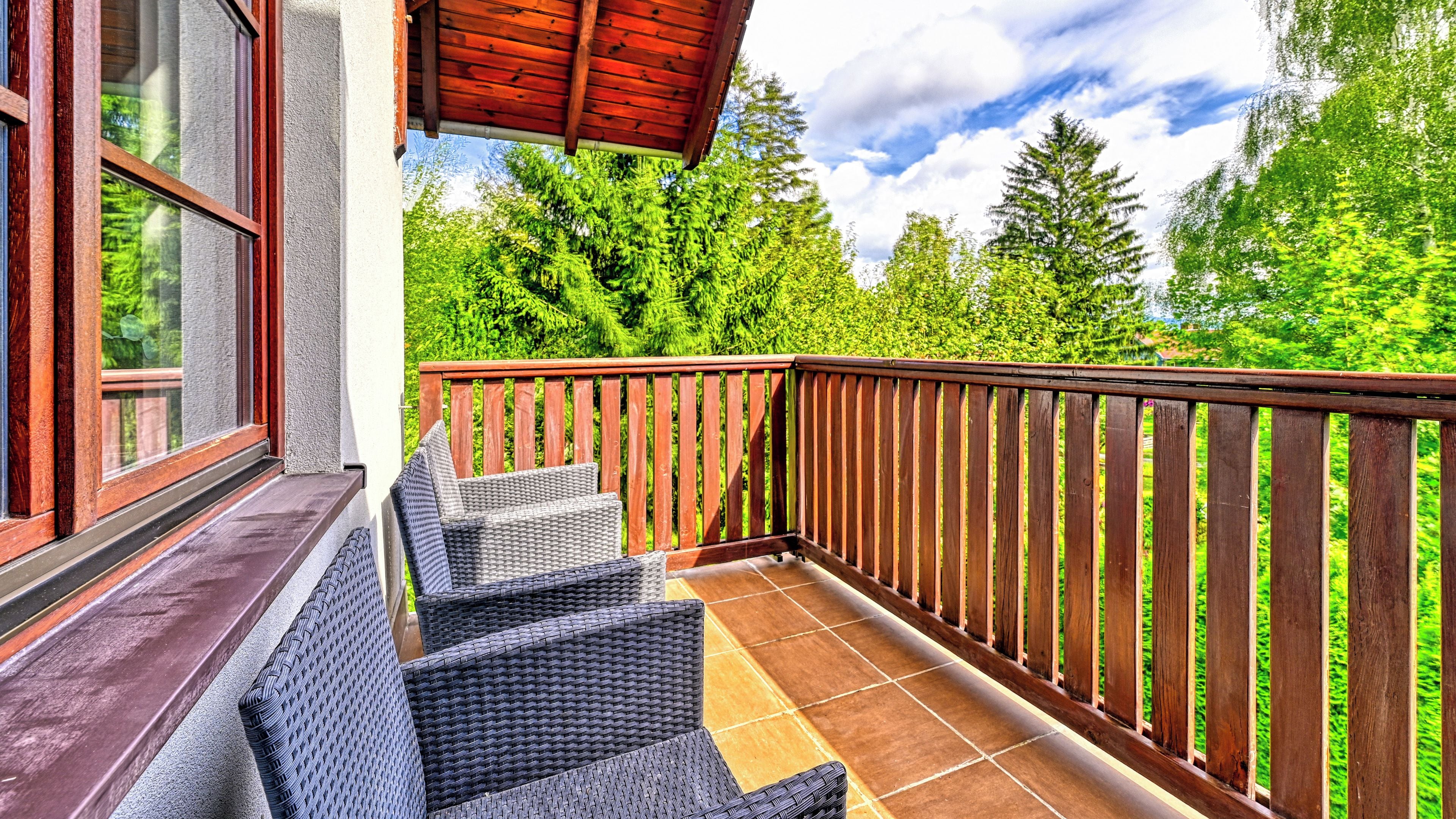 A balcony with wicker furniture and a wooden railing, overlooking a lush green landscape.