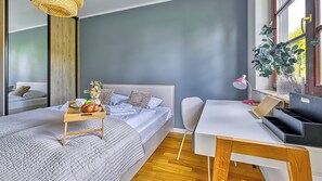 A modern bedroom with a bed, bedside table, desk, and a window with a plant. - Apartamenty Sun & Snow Okrzei (Karpacz)