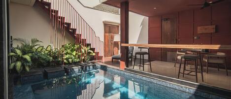 Ein moderner Poolbereich im Innenbereich mit einer Glaswand, einer Holztreppe und einer Bar mit Sitzgelegenheiten.