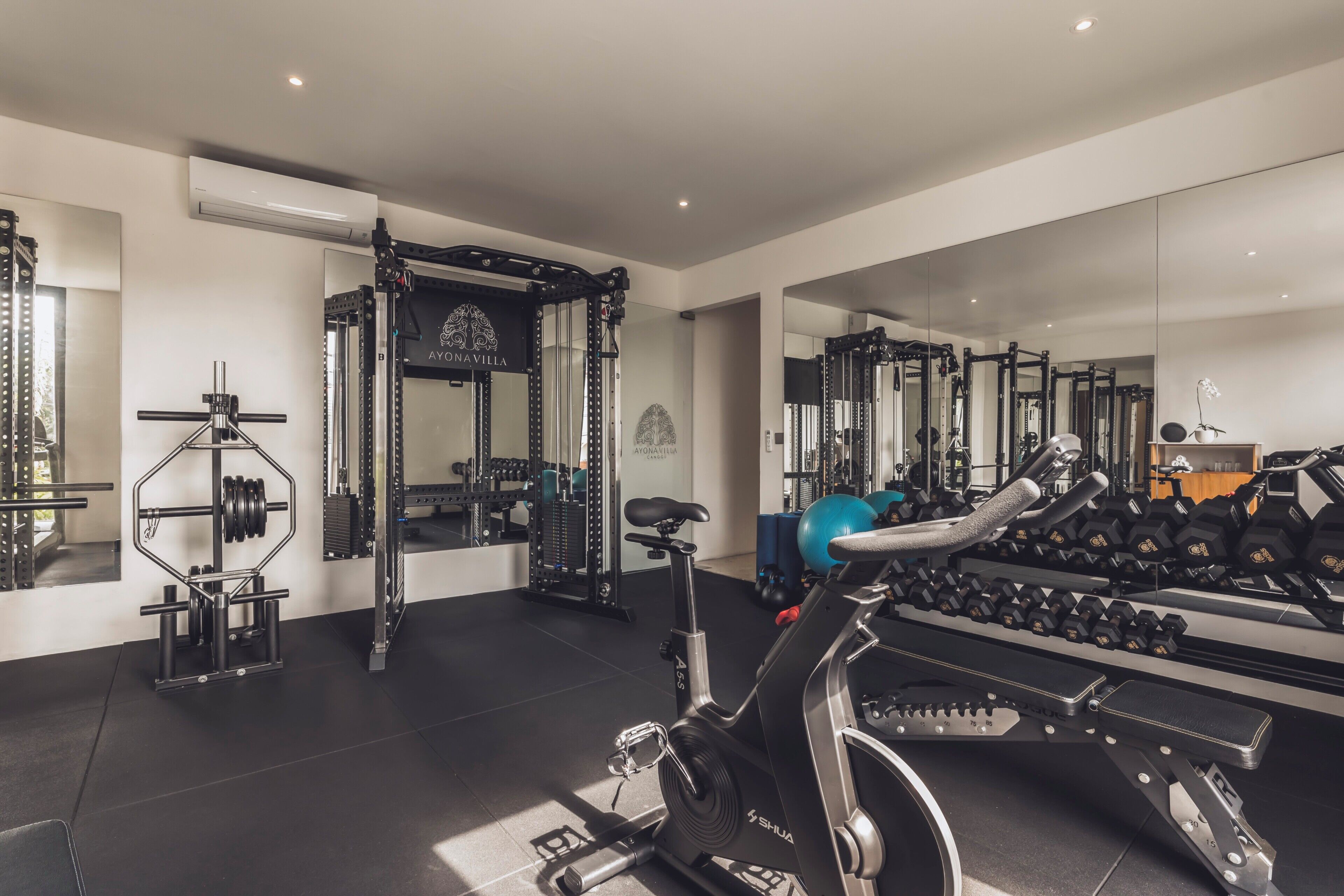 Ein Fitnessstudio mit verschiedenen Trainingsgeräten, darunter ein Ergometer, Kraftgeräte und Kurzhanteln.