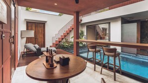 A modern interior with a pool, a round wooden table, and a staircase. - Ayona Villa Canggu by Ini Vie Hospitality (Canggu)