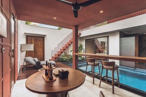 A modern interior with a pool, a round wooden table, and a staircase. - Ayona Villa Canggu by Ini Vie Hospitality (Canggu)