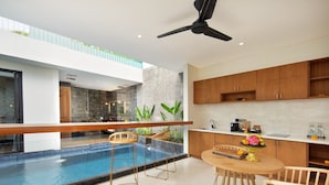 A modern kitchen with a pool, wooden bar stools, and a dining table. - Ayona Villa Canggu by Ini Vie Hospitality (Canggu)
