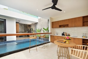 A modern kitchen with a pool, wooden bar stools, and a dining table. - Ayona Villa Canggu by Ini Vie Hospitality (Canggu)