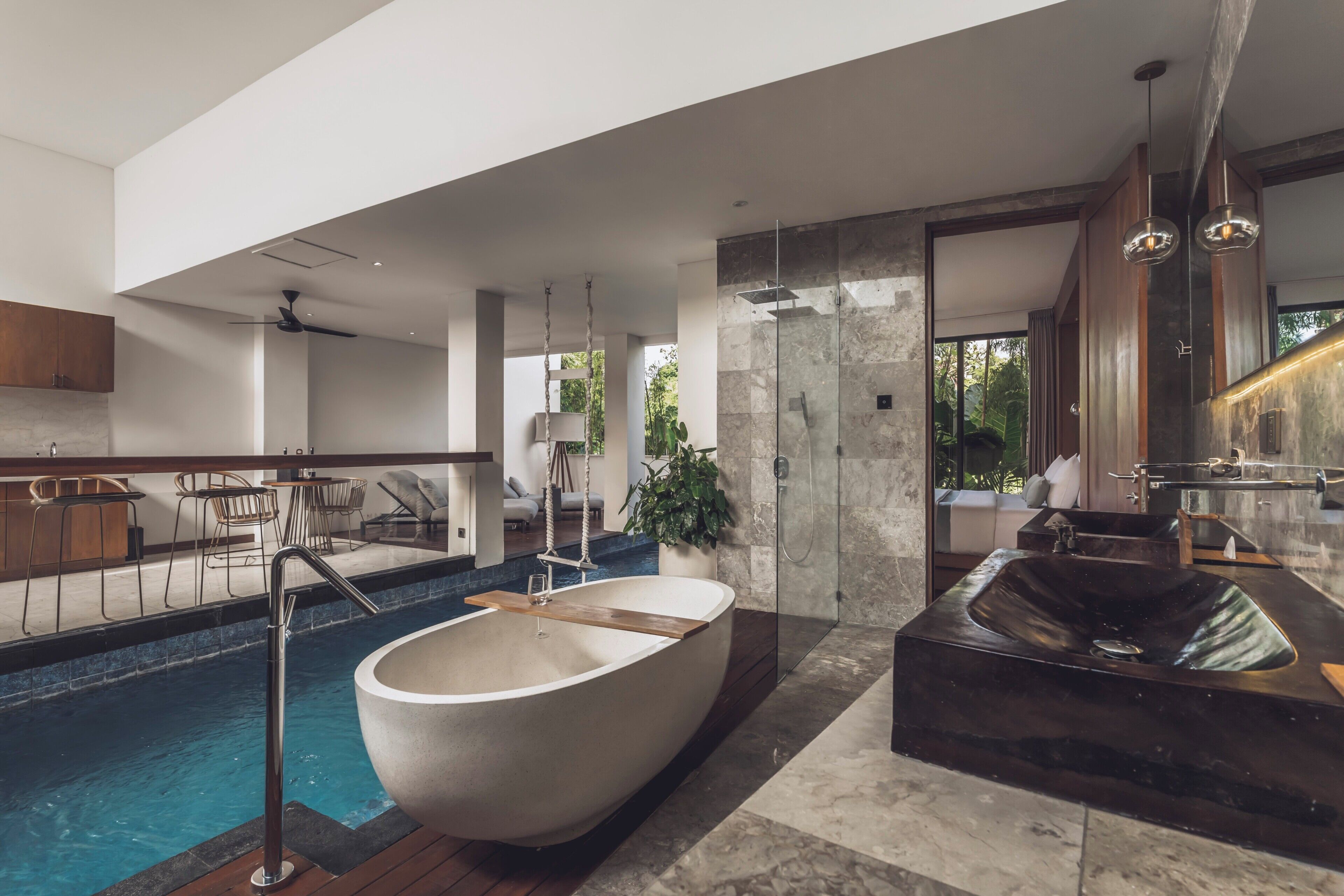 Een moderne badkamer met een groot bad, een aparte douche en een zwembad met glazen omheining.