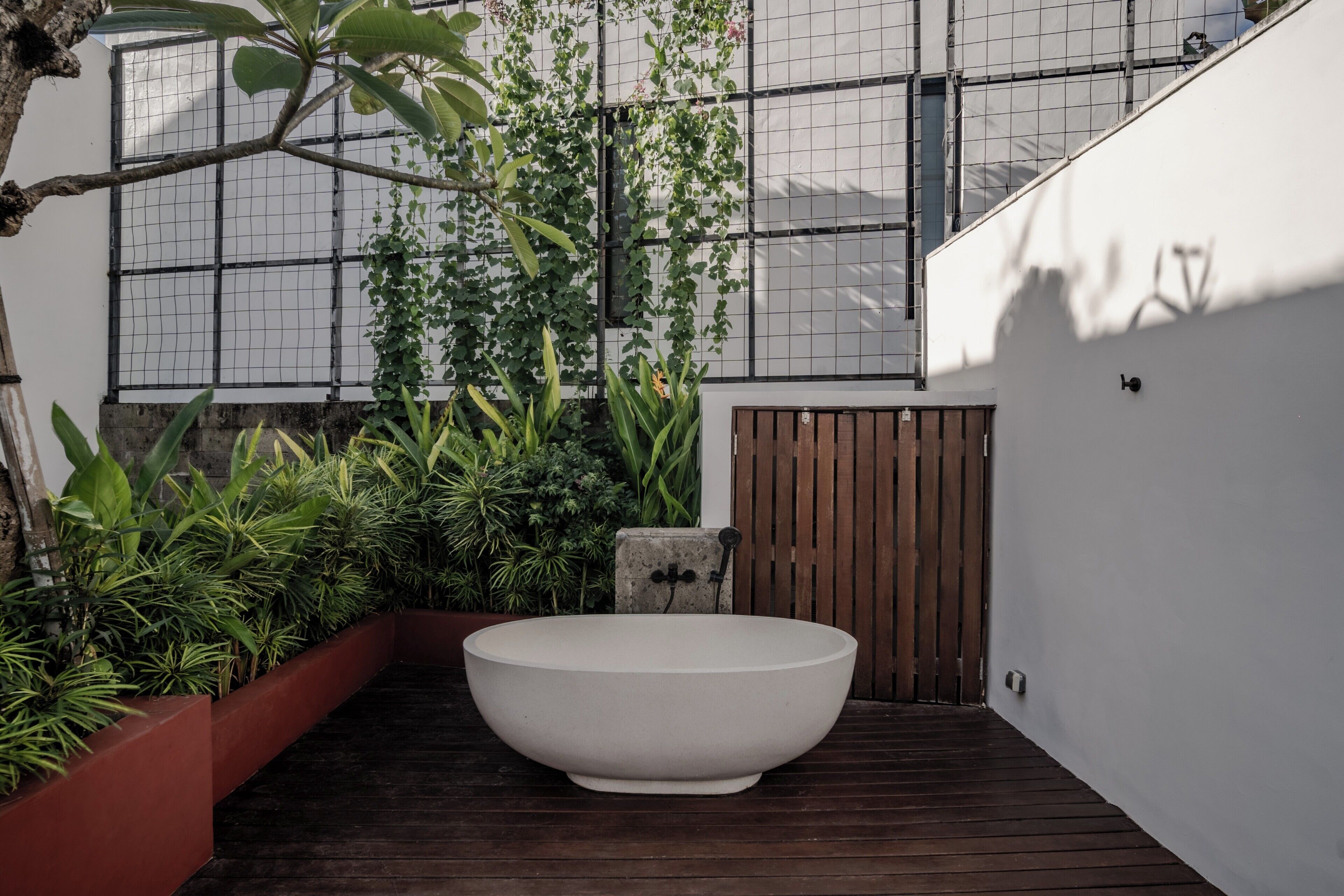 A modern outdoor space with a large white planter, wooden decking, and various green plants.