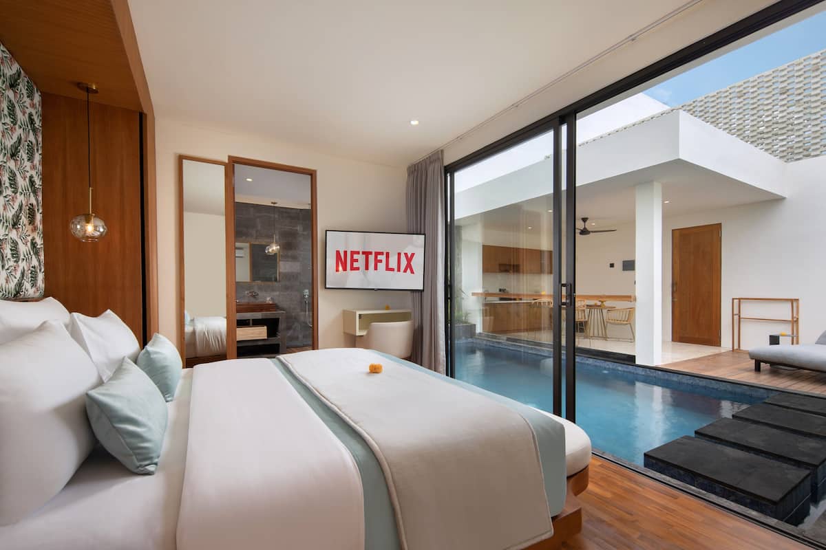 A modern hotel room with a large bed, a view of a swimming pool, and a sign for Netflix.