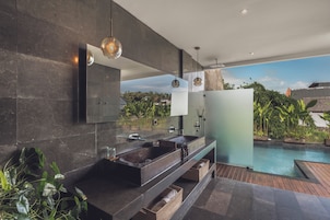 A modern bathroom with a large mirror, dark tiles, a sink, and a view of a swimming pool.