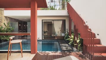 Un área moderna de piscina al aire libre con una terraza de madera, un espacio de descanso con una silla y una escalera que conduce a un nivel superior.