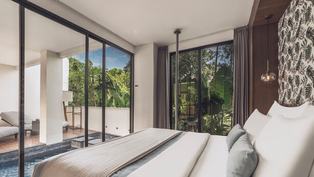 Habitación de hotel moderna con una cama grande, vistas a una piscina y un balcón con mobiliario exterior.