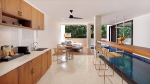 A modern kitchen with wooden cabinets, a bar area with stools, a built-in pool, and a seating area with a sofa and chairs. - Ayona Villa Canggu by Ini Vie Hospitality (Canggu)