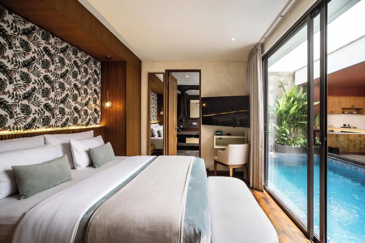 A modern hotel room with a large bed, a view of an indoor pool, and a bathroom with a shower and toilet.